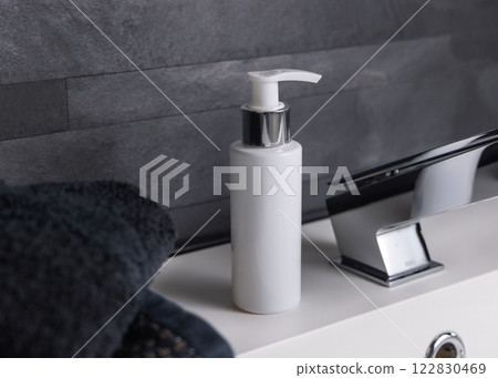 White cream bottle near black folded towels on basin in dark grey bathroom close up, cosmetic mockup White cream bottle near black folded towels on basin in dark grey bathroom close up, cosmetic mockup 122830469