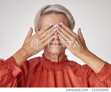 Senior, hands and covering eyes or face of mature woman suffering with a headache or eye strain while posing against a grey studio background. Elderly woman having problems with her vision or sight. 122830809