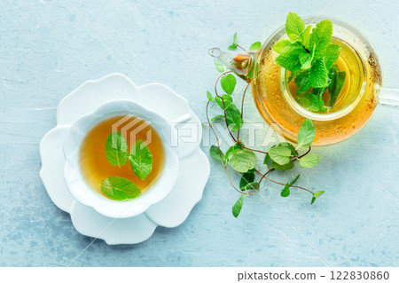 Mint tea. A cup of peppermint tea with fresh mint leaves and a tea pot Mint tea. A cup of peppermint tea with fresh mint leaves and a tea pot 122830860