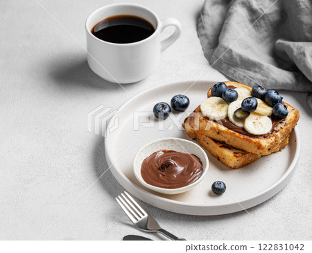 Toasted bread with chocolate cream, blueberries and banana on a plate on a light background Toasted bread with chocolate cream, blueberries and banana on a plate on a light background 122831042