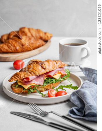 Croissant sandwich with ham, cheese, tomato  and arugula on a plate on a light background 122831056