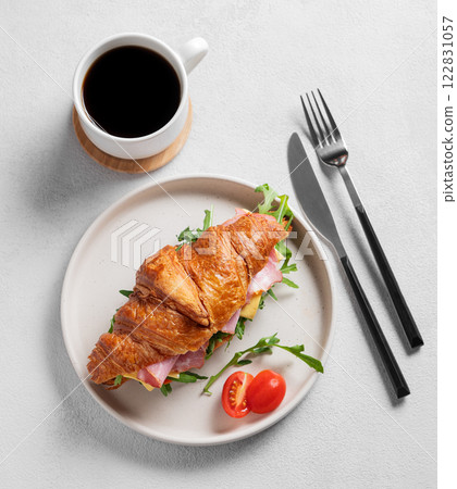 Croissant sandwich with ham, cheese, tomato  and arugula on a plate on a light background 122831057