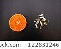 pills and capsules on black background and a half of orange 122831246