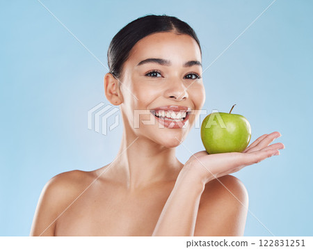 Wellness, health and beauty with woman and an apple for nutrition, detox and green diet against a blue background. Nutritionist, smile and fruit with happy female eating healthy for natural lifestyle 122831251