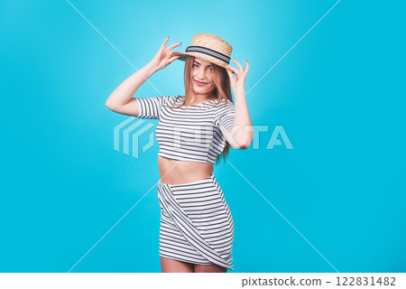 Attractive girl in a white and black stripes, hat, sunglasses, emotionally opened mouth on a bright blue background with a perfect body. Isolated. Studio shot Attractive girl in a white and black stripes, hat, sunglasses, emotionally opened mouth on a bright blue background with a perfect body. Isolated. Studio shot 122831482