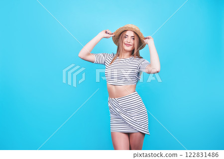 Attractive girl in a white and black stripes, hat, sunglasses, emotionally opened mouth on a bright blue background with a perfect body. Isolated. Studio shot 122831486