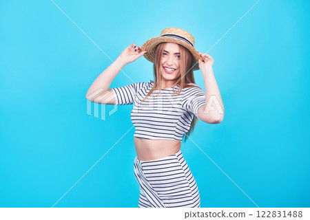 Attractive girl in a white and black stripes, hat, sunglasses, emotionally opened mouth on a bright blue background with a perfect body. Isolated. Studio shot 122831488