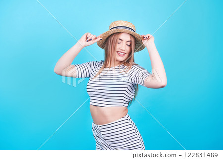 Attractive girl in a white and black stripes, hat, sunglasses, emotionally opened mouth on a bright blue background with a perfect body. Isolated. Studio shot 122831489