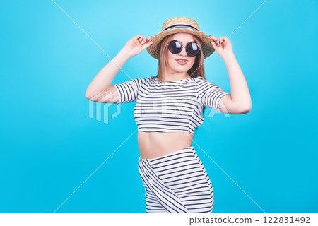Attractive girl in a white and black stripes, hat, sunglasses, emotionally opened mouth on a bright blue background with a perfect body. Isolated. Studio shot Attractive girl in a white and black stripes, hat, sunglasses, emotionally opened mouth on a bright blue background with a perfect body. Isolated. Studio shot 122831492