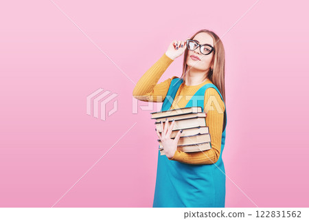 Happy cute girl in glasses holding in hands a pile of books isolated on colorful pink background Happy cute girl in glasses holding in hands a pile of books isolated on colorful pink background 122831562