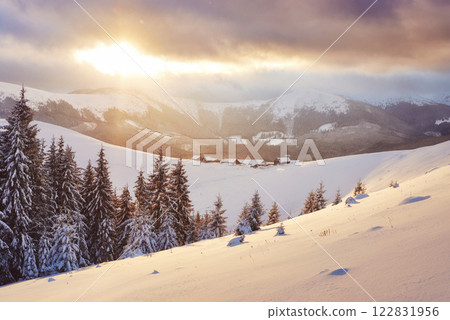 Majestic sunset at small village on a snowy hill under Ukrainian. Villages in the mountains in winter. Beautiful winter landscape. Carpathians, Ukraine, Europe 122831956