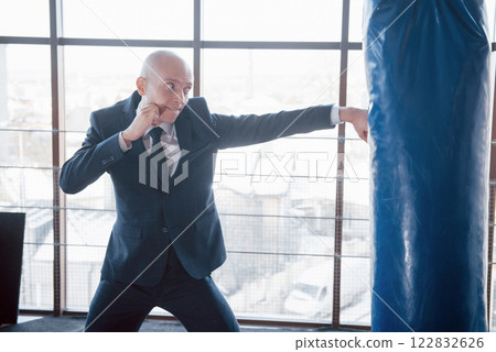 An angry bald businessman beats a boxing pear in the gym. concept of anger management 122832626