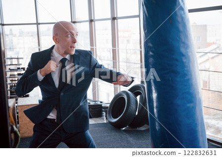 An angry bald businessman beats a boxing pear in the gym. concept of anger management 122832631