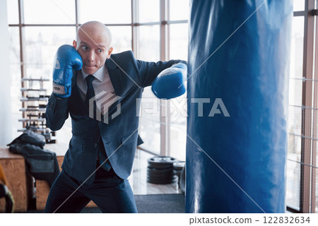 An angry bald businessman beats a boxing pear in the gym. concept of anger management 122832634