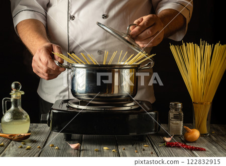 A chef skillfully prepares spaghetti, placing the long strands into a boiling pot on a stove. European cuisine A chef skillfully prepares spaghetti, placing the long strands into a boiling pot on a stove. European cuisine 122832915