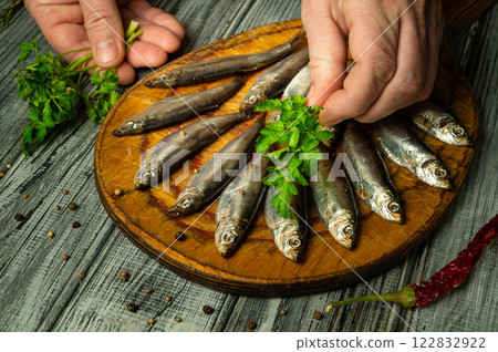 Hands delicately arrange fresh fish on a wooden platter, adding vibrant herbs or parsley. The rustic kitchen ambiance enhances the culinary artistry, inviting a feast of flavors Hands delicately arrange fresh fish on a wooden platter, adding vibrant herbs or parsley. The rustic kitchen ambiance enhances the culinary artistry, inviting a feast of flavors 122832922