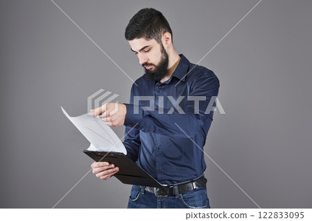 Concentrated young attractive businessman in blue shirt planning and writing in clipboard Concentrated young attractive businessman in blue shirt planning and writing in clipboard 122833095