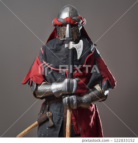 Medieval knight on grey background. Portrait of brutal dirty face warrior with chain mail armour red and black clothes and battle axe 122833152