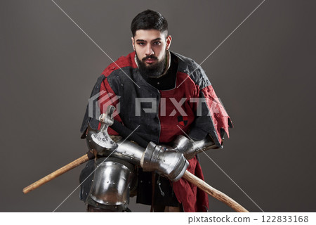 Medieval knight on grey background. Portrait of brutal dirty face warrior with chain mail armour red and black clothes and battle axe Medieval knight on grey background. Portrait of brutal dirty face warrior with chain mail armour red and black clothes and battle axe 122833168
