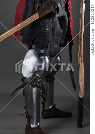 Medieval knight on grey background. Portrait of brutal dirty face warrior with chain mail armour red and black clothes and battle axe 122833219