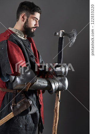 Medieval knight on grey background. Portrait of brutal dirty face warrior with chain mail armour red and black clothes and battle axe Medieval knight on grey background. Portrait of brutal dirty face warrior with chain mail armour red and black clothes and battle axe 122833220