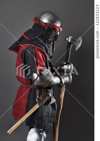 Medieval knight on grey background. Portrait of brutal dirty face warrior with chain mail armour red and black clothes and battle axe 122833223