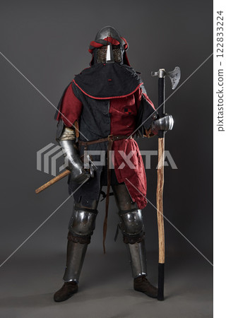 Medieval knight on grey background. Portrait of brutal dirty face warrior with chain mail armour red and black clothes and battle axe 122833224