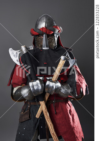 Medieval knight on grey background. Portrait of brutal dirty face warrior with chain mail armour red and black clothes and battle axe 122833228