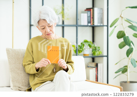 Senior woman holding a pension book in the living room Senior woman holding a pension book in the living room 122833279