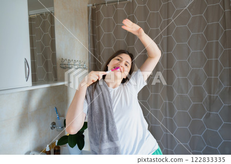 Girl happily dances and brushes her teeth, starting the day with a smile and good mood. Morning routine with fun: brushing and dancing in the bathroom. 122833335