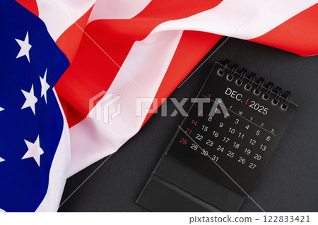 December 2025 black monthly desk calendar and United States of America flag. 122833421