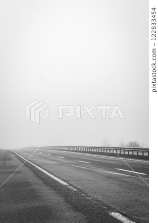 Empty highway in the fog, black and white. Bad weather on the road, monochrome. Road on foggy day in perspective with copy space. Driving conditions concept. Ghostly misty road. Caution and danger Empty highway in the fog, black and white. Bad weather on the road, monochrome. Road on foggy day in perspective with copy space. Driving conditions concept. Ghostly misty road. Caution and danger 122833454