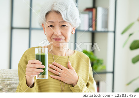 Senior woman drinking green juice in the living room Senior woman drinking green juice in the living room 122833459