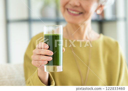 Senior woman drinking green juice in the living room Senior woman drinking green juice in the living room 122833460