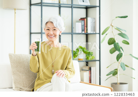 Senior woman drinking green juice in the living room Senior woman drinking green juice in the living room 122833463