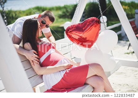 waiting baby. pregnant woman with beloved husband sit on a bench. Husband hand embraces a round belly wife. Parenthood. pregnant woman in a white dress in cherry with a red bow. close-up. nine months waiting baby. pregnant woman with beloved husband sit on a bench. Husband hand embraces a round belly wife. Parenthood. pregnant woman in a white dress in cherry with a red bow. close-up. nine months 122833487