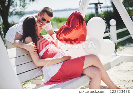 waiting baby. pregnant woman with beloved husband sit on a bench. Husband hand embraces a round belly wife. Parenthood. pregnant woman in a white dress in cherry with a red bow. close-up. nine months waiting baby. pregnant woman with beloved husband sit on a bench. Husband hand embraces a round belly wife. Parenthood. pregnant woman in a white dress in cherry with a red bow. close-up. nine months 122833488