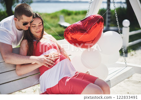 waiting baby. pregnant woman with beloved husband sit on a bench. Husband hand embraces a round belly wife. Parenthood. pregnant woman in a white dress in cherry with a red bow. close-up. nine months waiting baby. pregnant woman with beloved husband sit on a bench. Husband hand embraces a round belly wife. Parenthood. pregnant woman in a white dress in cherry with a red bow. close-up. nine months 122833491