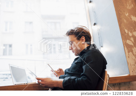 Relaxed young professional surfing the Internet on his laptop in a cafe 122833628