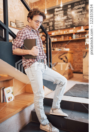 Talented young man in casual shirt drawing sketch in notebook enjoying leisure time in coffee shop.Skilled student writing down homework in notepad sitting in coworking 122833634