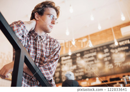 Thoughtful young man is sitting in confectionery shop. She is drinking coffee while waiting for someone 122833641