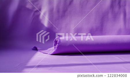 Purple fabric is rolled up on a table. The color of the fabric is very bright and vivid 122834008