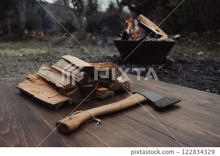 Hatchet, firewood on a table and a bonfire in the background 122834329