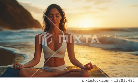 Woman meditating on a beach at sunset with the ocean in the background 122835485