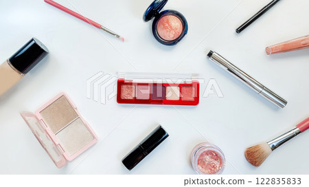 Flat lay of beauty products on a white background, featuring eyeshadow, lipstick, foundation, and makeup brushes. 122835833