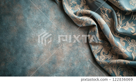 Blue and gold fabric with a floral pattern is draped over a wall. The fabric is folded and draped in a way that creates a sense of movement and flow 122836069