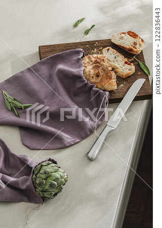 Sliced bread on wooden board, artichoke and stainless still kitchen knife. Kitchen aesthetic concept Sliced bread on wooden board, artichoke and stainless still kitchen knife. Kitchen aesthetic concept 122836443