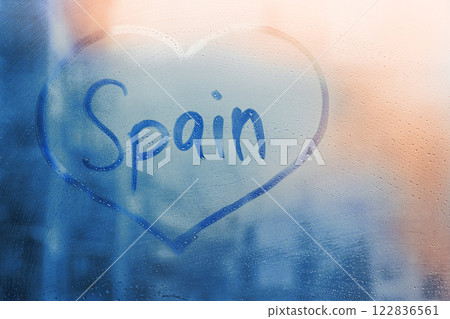 Foggy glass on window with written finger word Spain in heart doodle shape on wet blue sunset window Foggy glass on window with written finger word Spain in heart doodle shape on wet blue sunset window 122836561