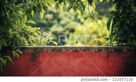 Red wall with a green tree in the background. The tree is in full bloom and the leaves are lush and green. The wall is a stark contrast to the vibrant green of the tree, creating a sense of calm 122837110
