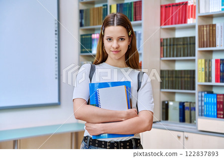 Portrait of teenage student girl with backpack in high school library classroom 122837893